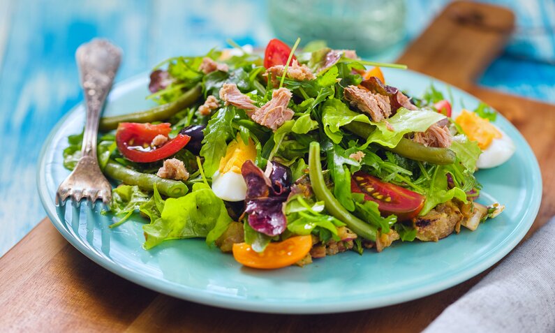 Auf einem blauen Teller ist ein reichhaltiger Salat, bestehend aus Thunfisch, Bohnen und grünem Salat, angerichtet. | © Getty Images / kajakiki