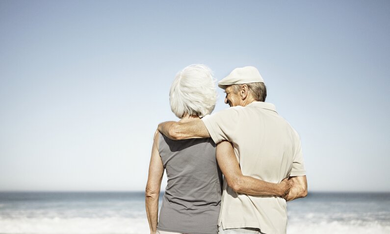 Seniorenpärchen steht Arm in Arm am Strand | ©  Getty Images / Roger Wright