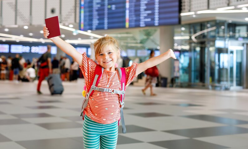 Ein Kind steht am Flughafen und hält seinen Reisepass in die Luft | ©  Getty Images / romrodinka