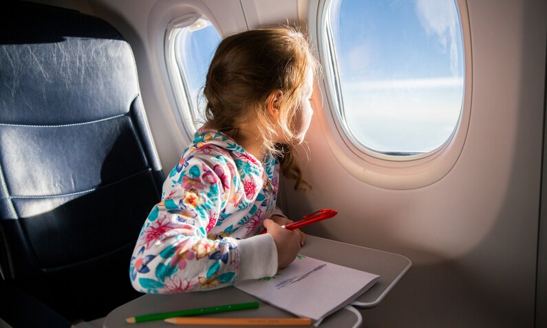 Kind sitzt in Flugzeug, malt und schaut dabei aus dem Fenster | ©  Getty Images / Suzi Media Production