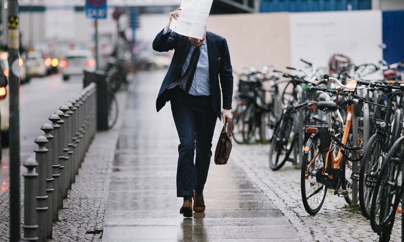 Mann läuft in Anzug durch den Regen und hält sich eine Akte über den Kopf | ©  Getty Images / Willie B. Thomas