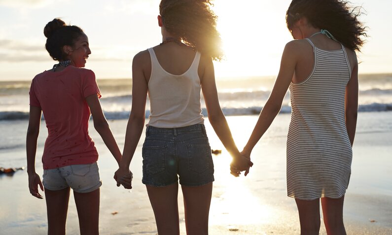 3 Jugendliche halten sich am Strand an der Hand  | ©  Getty Images / Klaus Vedfelt