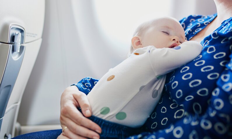 Baby liegt schlafend im Arm der Mutter in einem Flugzeug | ©  Getty Images / encrier