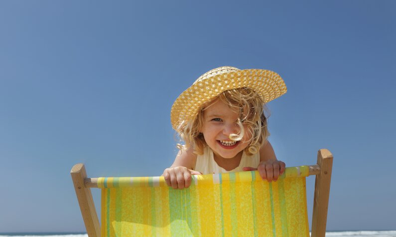 Kleines Mädchen guckt über Liegestuhl am Strand | ©  Getty Images / Peter Cade