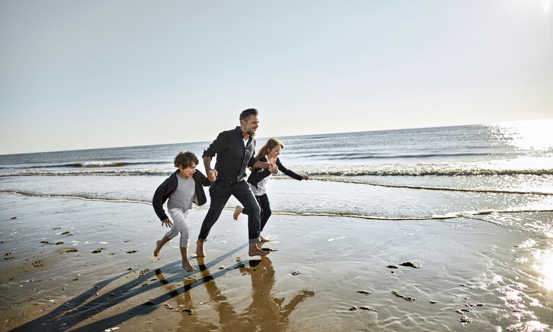 Vater rennt mit seinen zwei Kindern am Nordseestrand | ©  Getty Images / Oliver Rossi