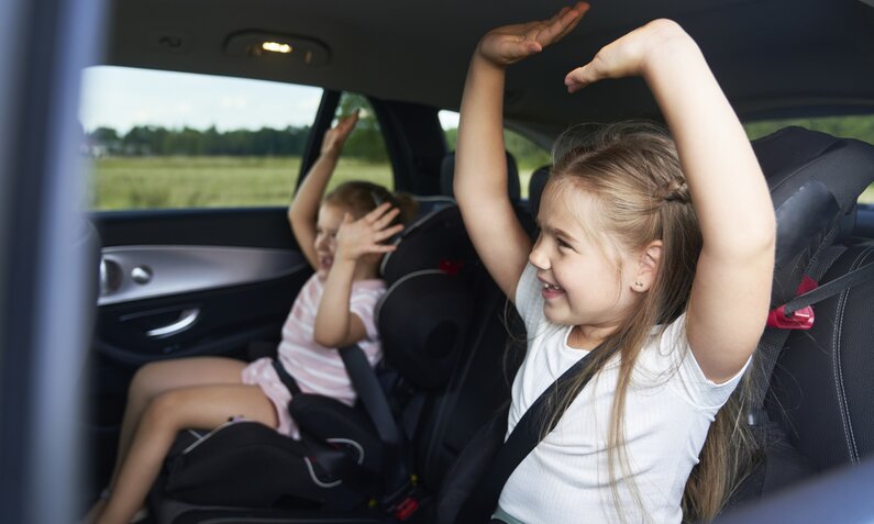 Kinder freuen sich auf der Rückbank eines Auto | ©  Getty Images / gpointstudio