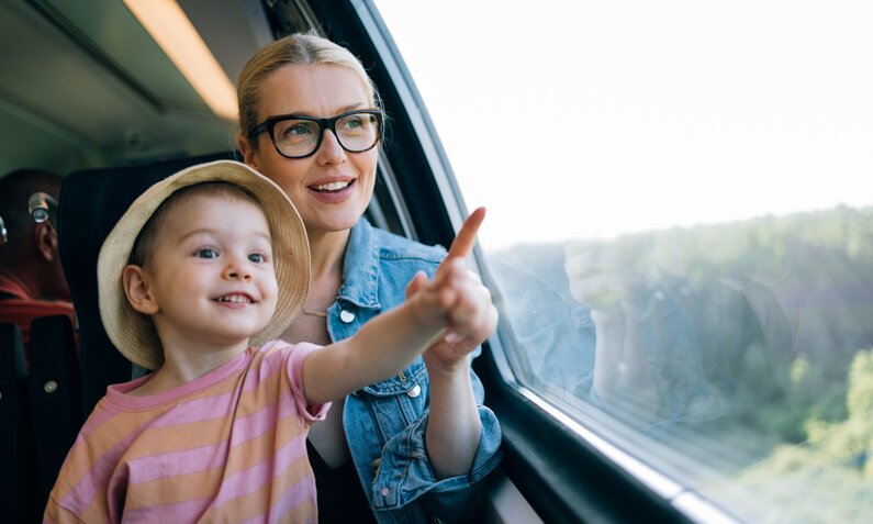 Frau sitzt mit Kind in der Bahn und schaut aus dem Fenster  | ©  Getty Images / miniseries