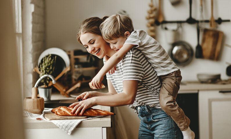 Frau mit Kind schneiden Brot in der Küche auf. | © Getty Images / evgenyatamanenko