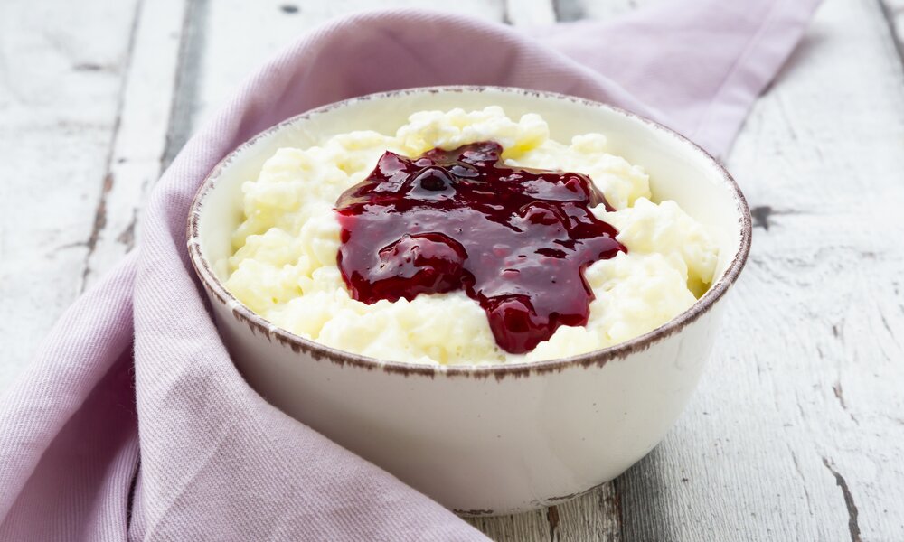 Milchreis mit Kirschen in einer weißen Schüssel auf rosa Untergrund. | © Getty Images / Westend61