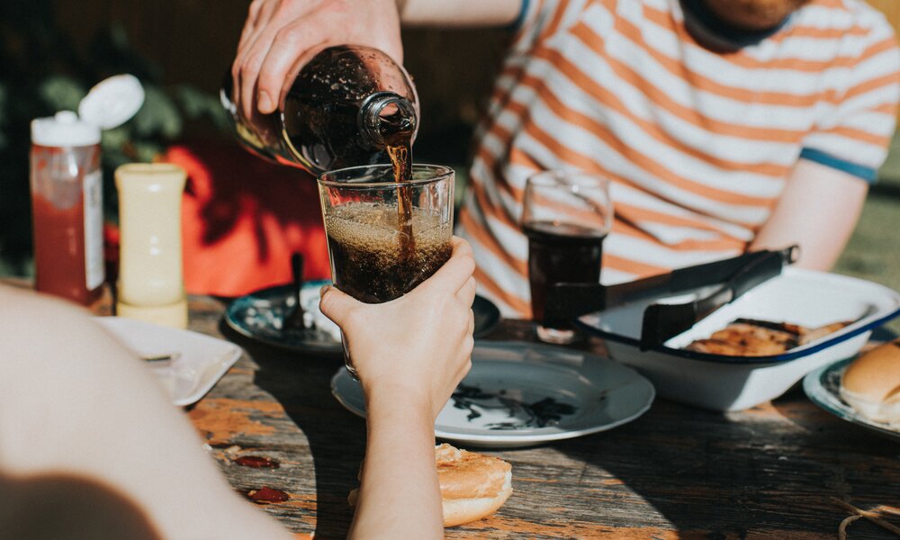 Mann im gestreiften T-Shirt schenkt einer Frau am Tisch Cola in ihr Glas. | © Getty Images / Catherine Falls Commercial