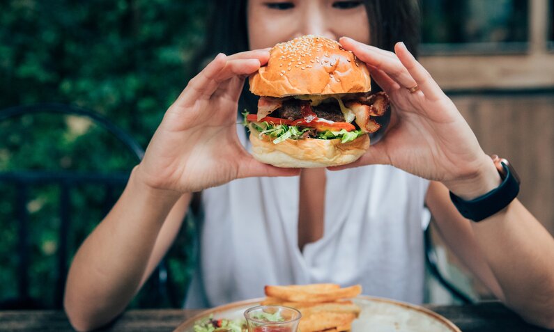 Asiatische Frau hält einen Burger in beiden Händen in die Kamera. | © Getty Images / Oscar Wong