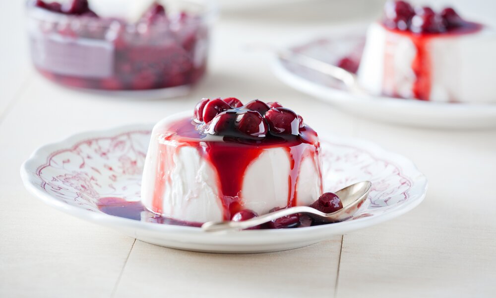 Auf einem englischen Teller ist eine Panna Cotta beträufelt mit Kirschen und Kirschsaft angerichtet. | © Getty Images / mpessaris
