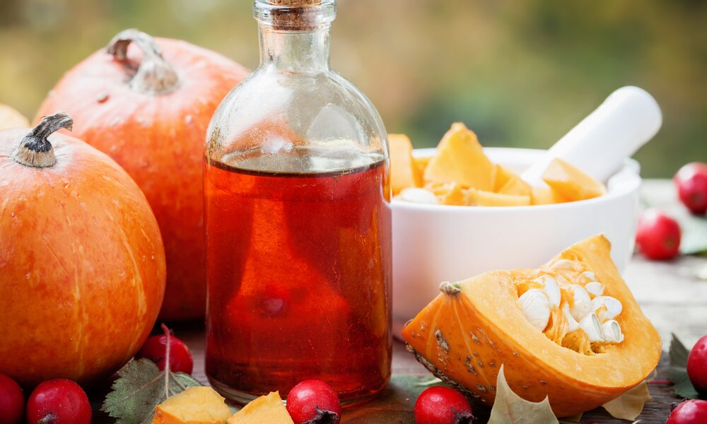 Eine Flasche befüllt mit Öl steht im Vordergrund vor aufgeschnittenen Kürbissen. | © Getty Images / ChamilleWhite