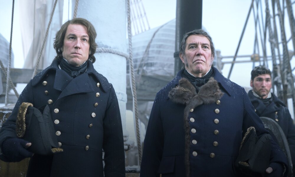 Ciaran Hinds und eine Co-Star stehen in einer Szene aus der Serie "The Terror" in Offiziersuniformen an Deck und blicken ernst | © 2017 AMC Film Holdings LLC. All Rights Reserved.