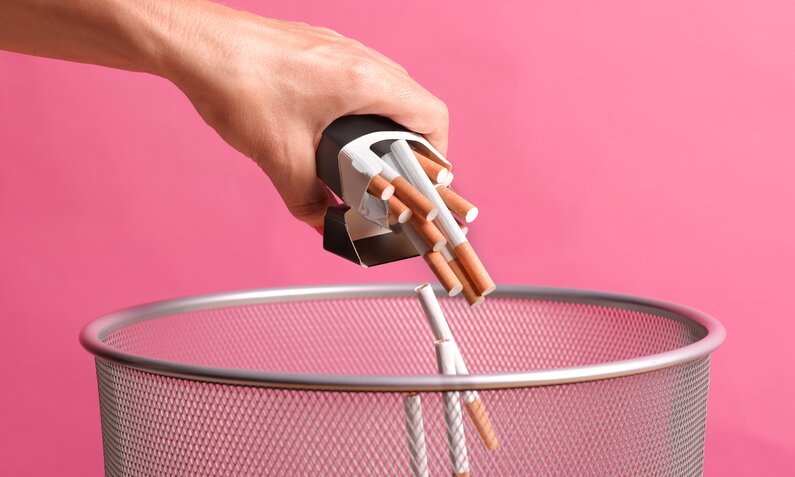 Frauenhand wirft Zigaretten in einen Mülleimer vor pinkem Hintergrund. | © Getty Images /Peter Dazeley