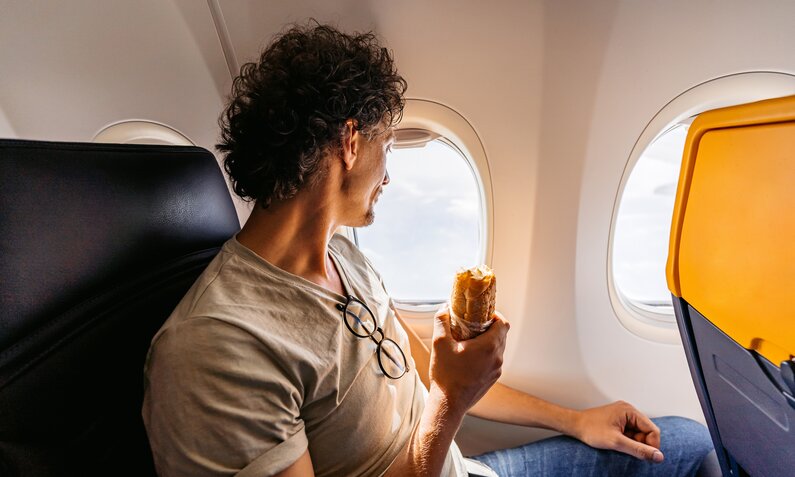 Mann isst Baguette im Flugzeug | ©  Getty Images / urbazon