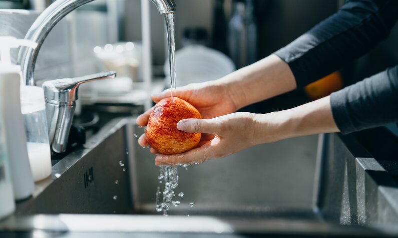 Frauenhänge waschen einen Apfel unter fließenden Wasser ab. | © Getty Images / d3sign