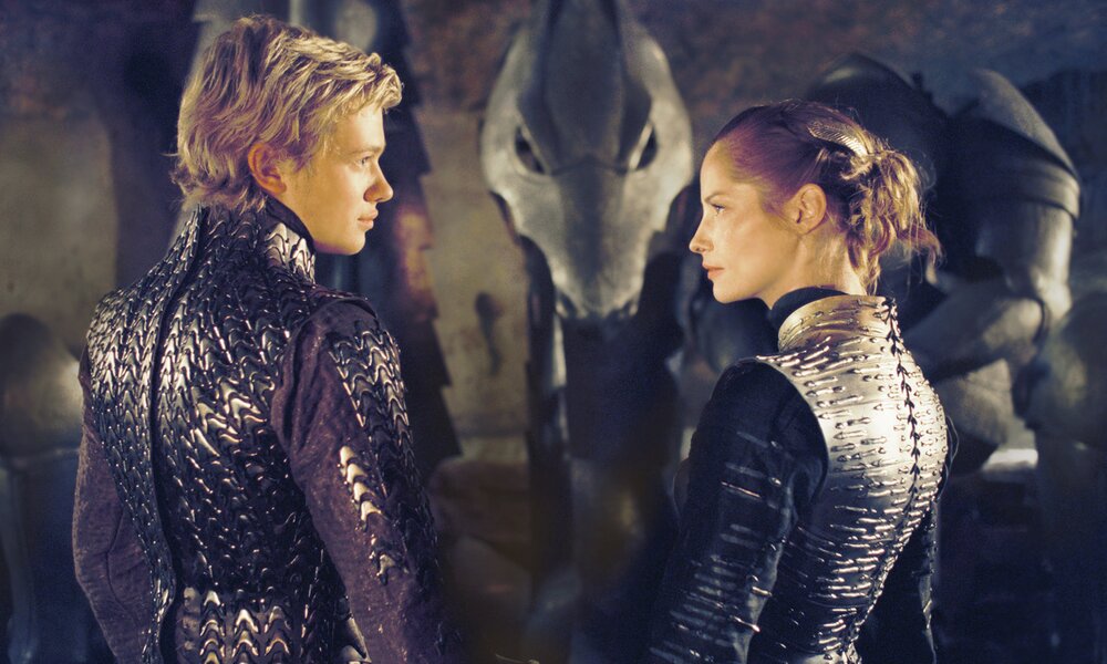 Edward Speleers und Sienna Guillory in silbernen Rüstungen stehen mit dem Rücken zum Betrachter in einem dunklen Raum und unterhalten sich in einer Szene aus dem Kinofilm "Eragon" | © ddp images/0th Century Fox/David Appleby