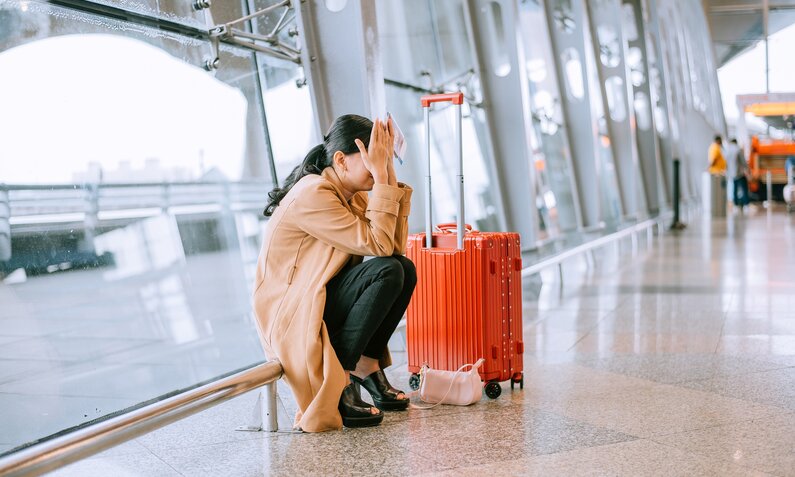 Frau sitzt am Flughafen und hält sich die Hände vor das gesicht | ©  Getty Images / KSChong