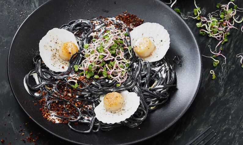 Schwarze Spaghetti angerichtet in einem weißen Teller und garniert mit Kresse. | © Getty Images / Eugene Mymrin