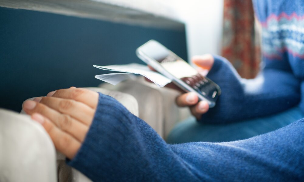 Frau fasst die Heizung an, in der anderen Hand hält sie ein Smartphone | ©  Getty Images / ArtMarie
