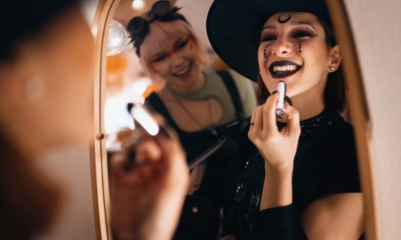 Frau schminkt sich vor dem Spiegel als Hexe | ©  Getty Images / SrdjanPav