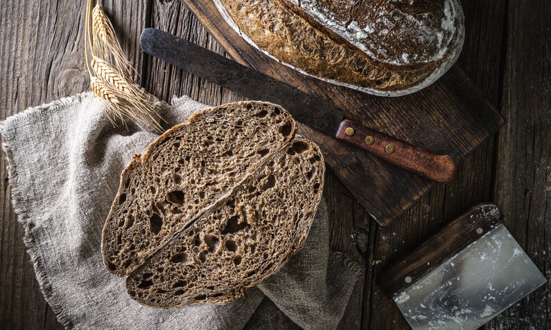 Brotlaib, aufgeschnitten, daneben 2 Scheiben Brot, angerichtet auf dunklem Untergrund. | © Getty Images / MEDITERRANEAN