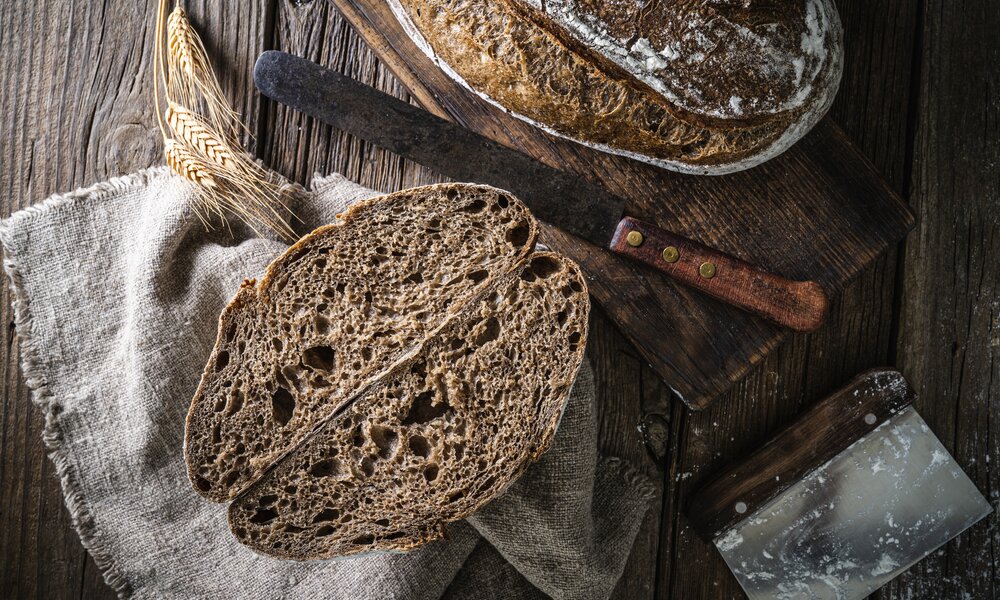 Brotlaib, aufgeschnitten, daneben 2 Scheiben Brot, angerichtet auf dunklem Untergrund. | © Getty Images / MEDITERRANEAN
