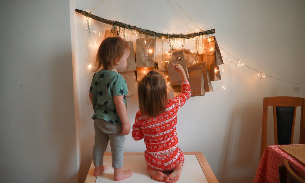 Zwei kleine Kinder stehen vor einem selbstgebastelten Adventskalender | © Getty Images / Natalia Lebedinskaia