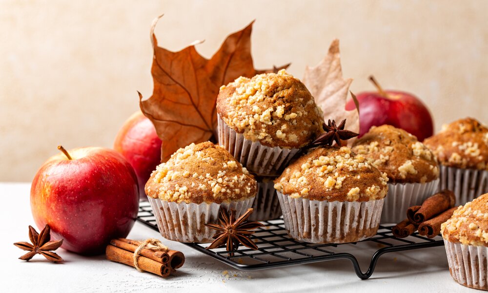 Apfelmuffins auf einem Gitterbrett, hinterlegt mit Zimtstangen und Herbstblättern. | © Getty Images / Olga Mazyarkina