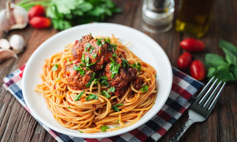 Auf einer Tischdecke angerichteter Teller mit Spaghetti und Hackbällchen, garniert mit Petersilie. | © Getty Images / MixitIstock