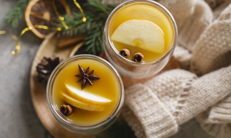 Zwei Gläser gefüllt mit orangem Inhalt und garniert mit einer Apfelscheibe und Sternanis in weihnachtlicher Umgebung. | © Getty Images / Alexandr Kolesnikov