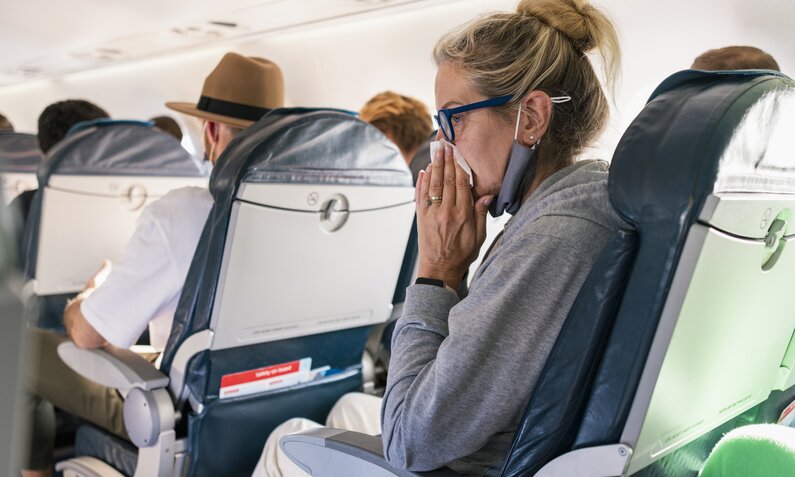 Frau schnäutzt sich im Flugzeug die Nase | ©  Getty Images / SolStock