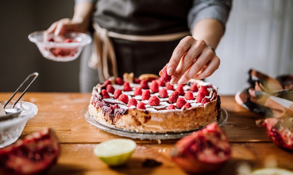 Frauenhände streuen Puderzucker über Kuchen. | © Getty Images / Pekic