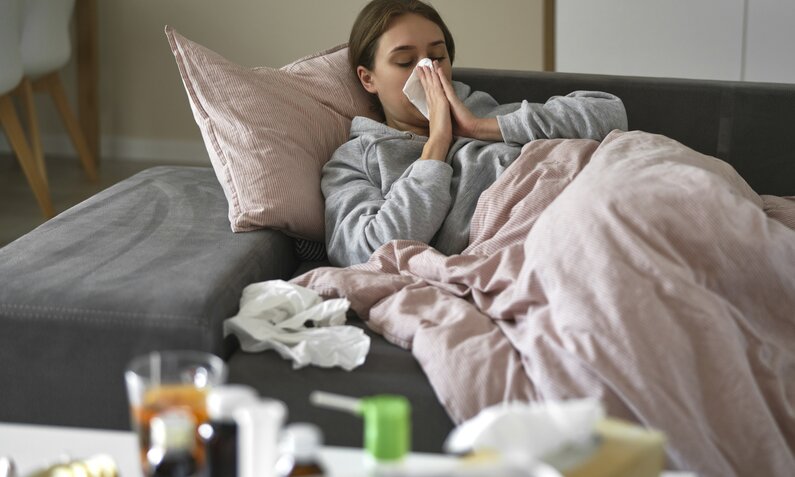 Frau liegt Krank auf der Couch und putzt sich die Nase | ©  Getty Images / gpointstudio