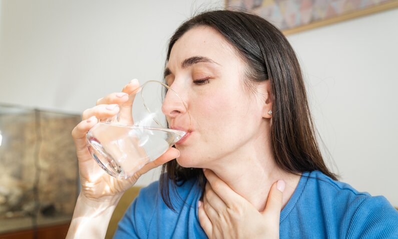 Frau hat Halsschmerzen und trinkt ein Glas Wasser | ©  Getty Images / Cate M