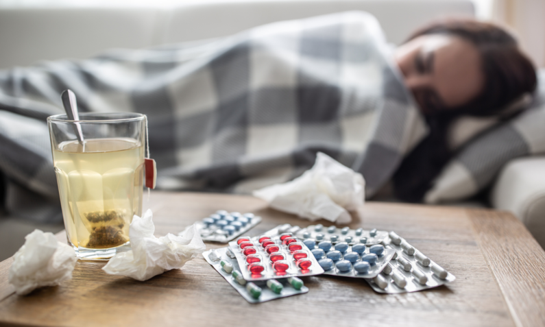 Frau liegt mit Erkältung auf dem Bett, vor ihr Medikamente und Tee | ©  Getty Images / SimpleImages