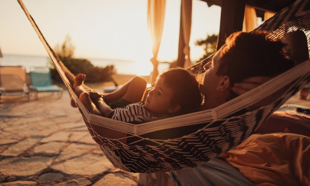 Mann und Kind in Hängematte beobachten den Sonnenuntergang | ©  Getty Images / AleksandarNakic