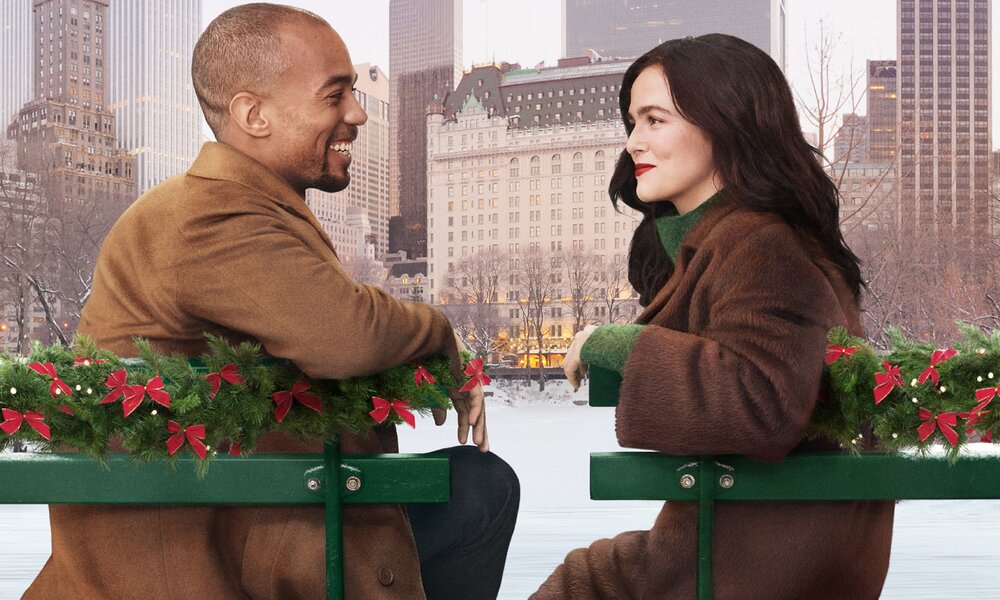 Kendrick Sampson und Zoey Deutch sitzen sich auf dem Plakat für den Prime Video Film "Weihnachtsgeschenke von Tiffany" auf einer Bank draußen gegenüber, im Hintergrund ist die winterliche Stadtkulisse von New York zu sehen | © Amazon Prime Video