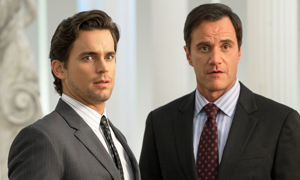 Nahaufnahme von Matt Bomer als Neal Caffrey und Tim DeKay als Peter Burke, die in einer Szene der Serie "White Collar" nebeneinander in einem hellen Raum stehen. | © Getty Images//USA Network