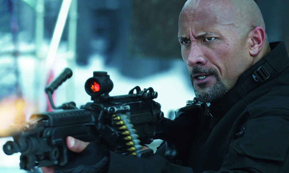 Dwayne Johnson mit schwerer Waffe im Anschlag in einer düsteren Szene aus dem Kinofilm "Fast & Furious 8" | © ddp images/Capital Pictures