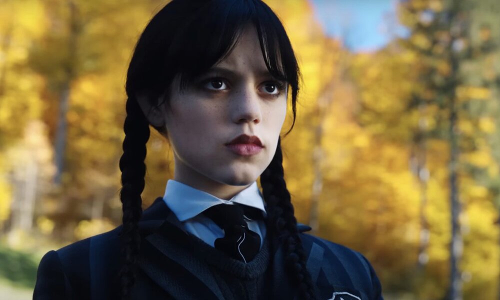 Jenny Ortega steht in einer Szene der Netflix-Serie "Wednesday" draußen in ihren schwarzen Kleidern vor einem leuchtend gelben Herbstwald. | © Netflix