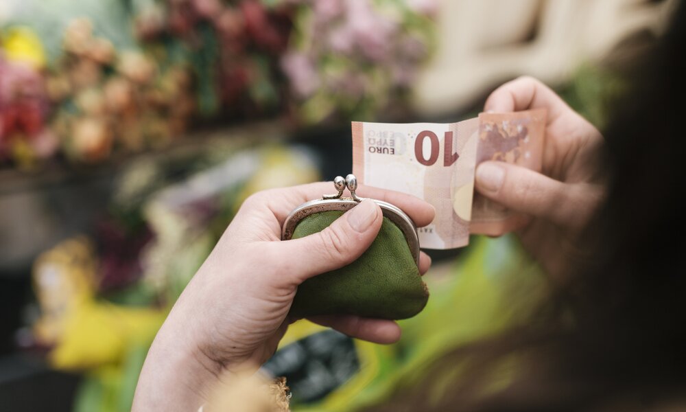 Frau holt 10€ Schein aus dem Portemonnaie | ©  Getty Images / Hinterhaus Productions