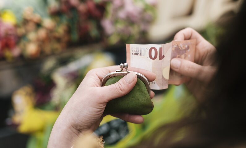 Frau holt 10€ Schein aus dem Portemonnaie | ©  Getty Images / Hinterhaus Productions