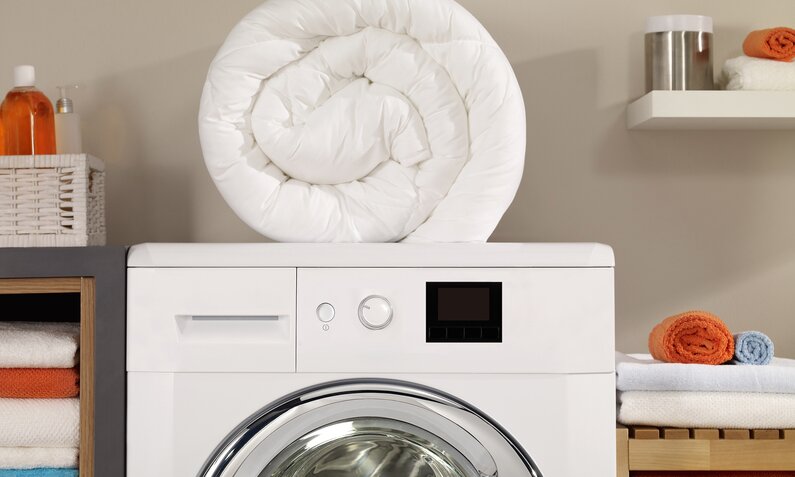 Gerollte Bettdecke liegt auf einer Waschmaschine | ©  Getty Images / gerenme