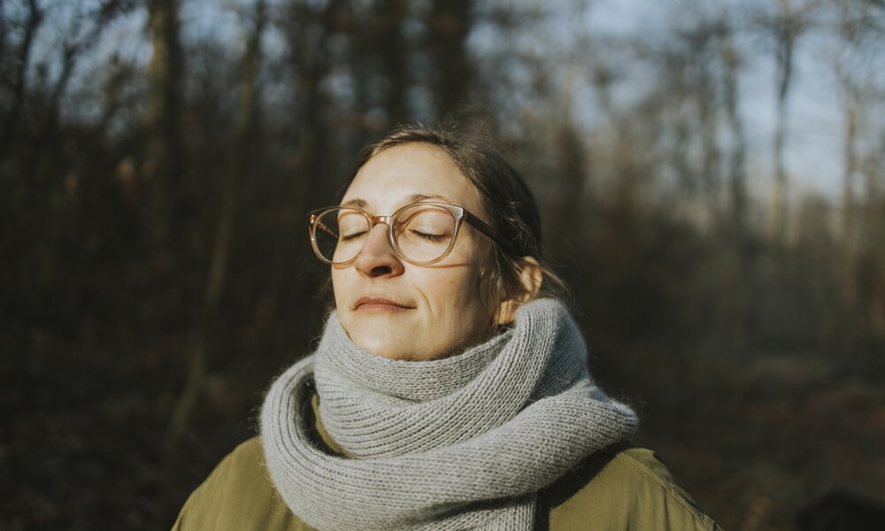 Frau mit Brille steht in Sonne im Winter mit geschlossenen Augen. | © Getty Images / Westend61