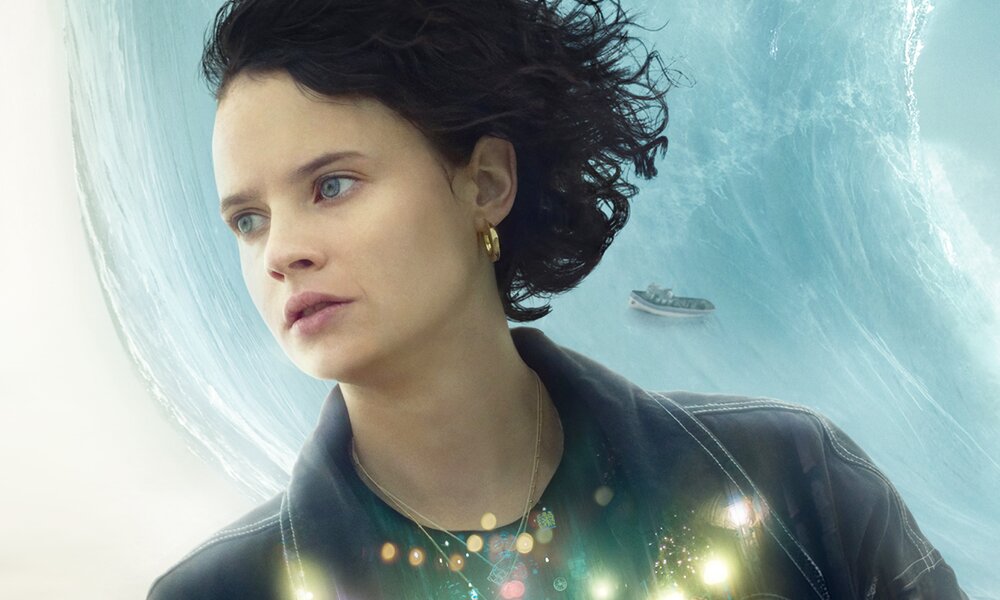  Jana McKinnon mot wehendem dunklen Haaren vor einem Hintergrund mit Meer, Boot und Strand auf dem Plakat zum Prime Video Film "Silber und das Buch der Träume" | © Amazon Studios/Prime Video