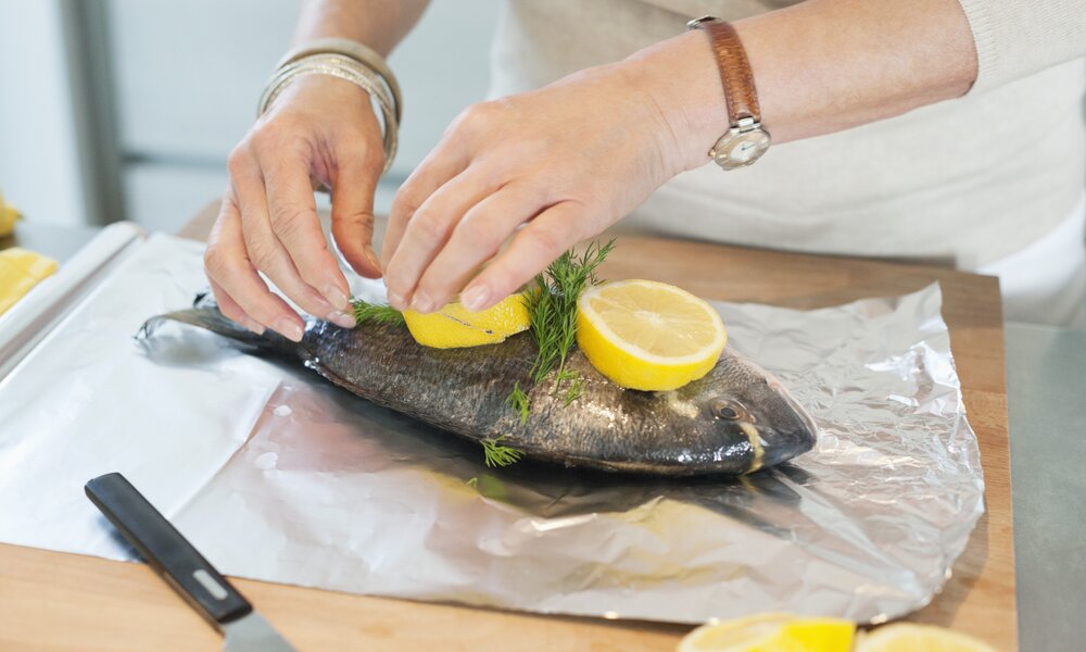 Frauenhänge wickeln einen frischen Fisch in Alufolie. | © Getty Images / Fabrice LEROUGE