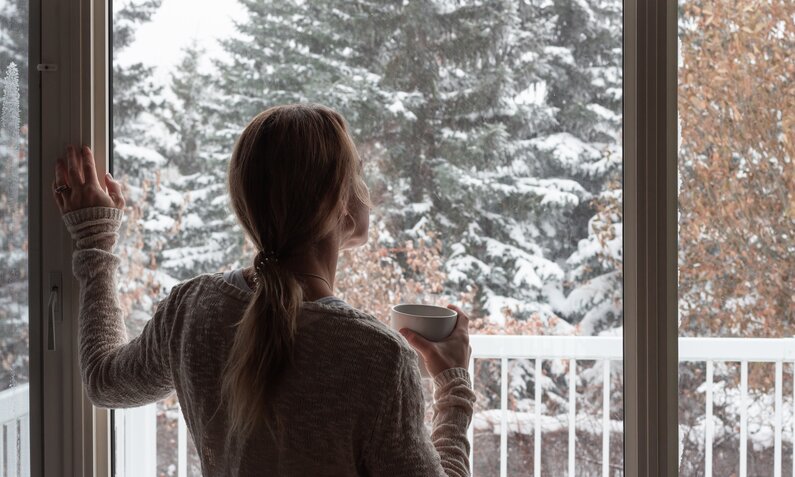 Frau steht bei geöffneten Fenster im Winter. | © Getty Images / Kara Gebhardt