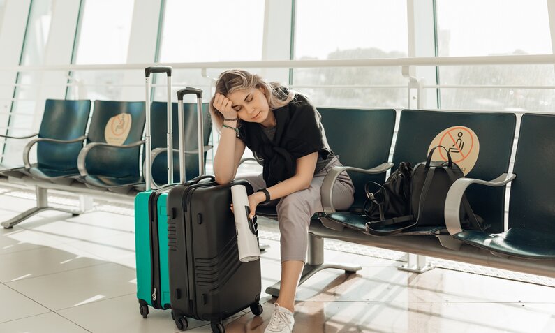  Frau sitzt erschöpft und enttäuscht am Flughafen | ©  Getty Images / Tatsiana Volkava